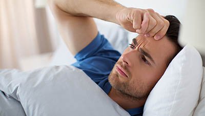 Мужчина лежит в кровати положив руку на лоб